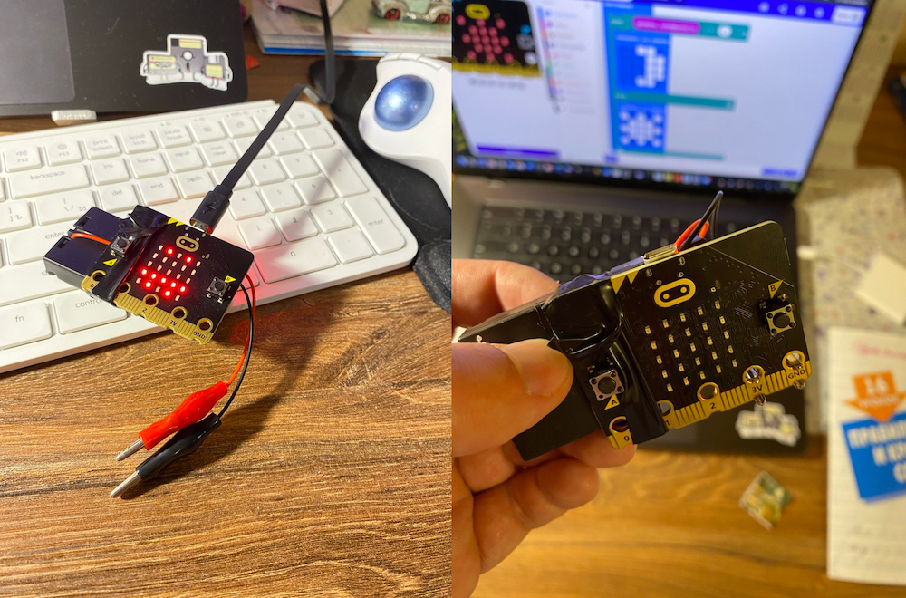 На изображении показаны две фотографии микроконтроллера BBC micro:bit. На левой части фото устройство лежит на белой клавиатуре, к нему подключён USB-кабель и аккумулятор, а также провода с крокодилами. На правой части крупным планом рука держит тот же micro:bit, а на заднем плане видны ноутбук с открытой программой для программирования и блокнот на столе. Всё действие происходит в помещении, на деревянном столе.